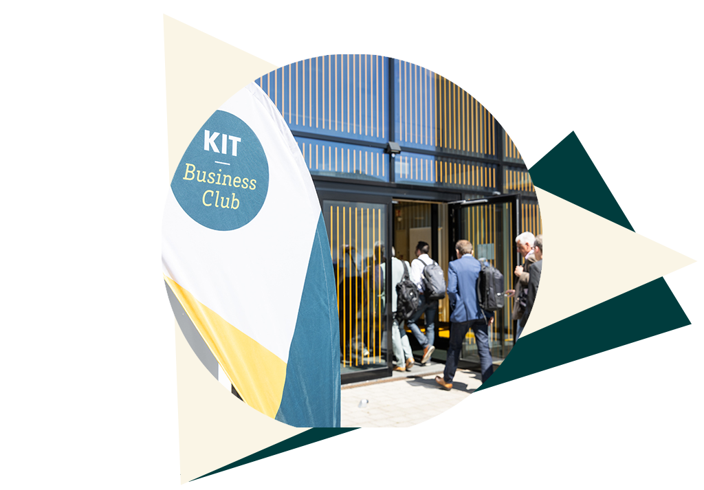 Personen betreten ein Gebäude neben einer Fahne des KIT Business Clubs.