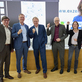 Eine Gruppe von Menschen posiert lächelnd vor einer Präsentation.