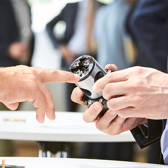 Zwei Personen untersuchen ein technisches Bauteil bei einer fachlichen Besprechung